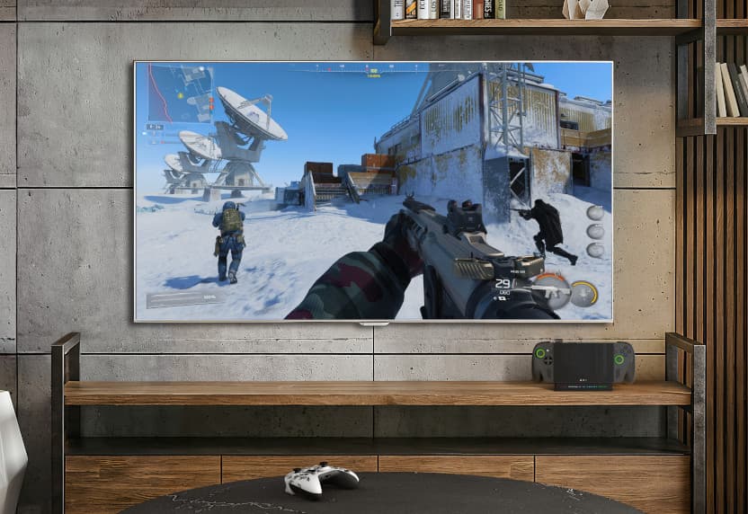ROG Xbox Ally X handheld docked on a shelf below a TV showing gameplay